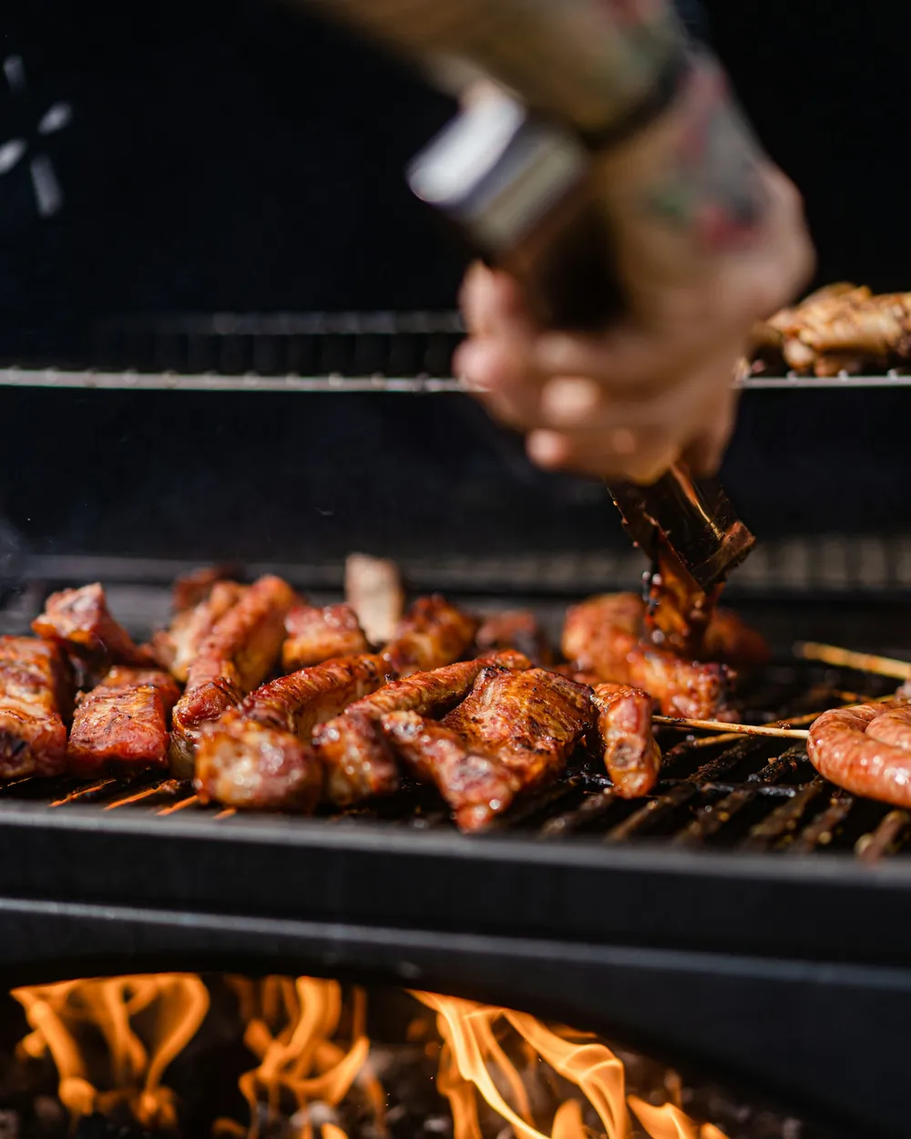 Mão temperando carnes na grelha sobre a brasa acesa com sal de parrilla